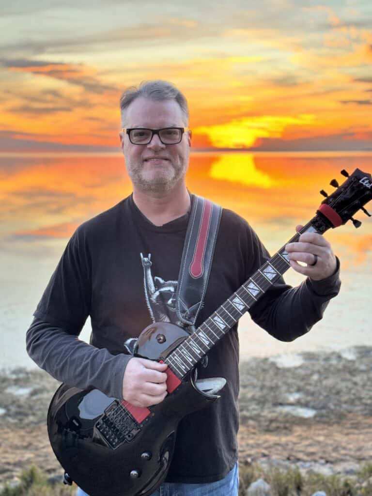 Guitarist holding an electric guitar during sunset at the beach.